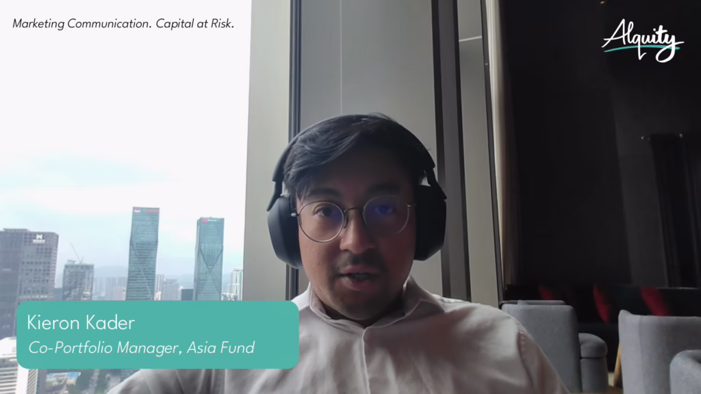 Kieron Kader, Co-Portfolio Manager of Alquity's Asia Fund, speaking on a video call with headphones on, city skyline visible through the window behind him.