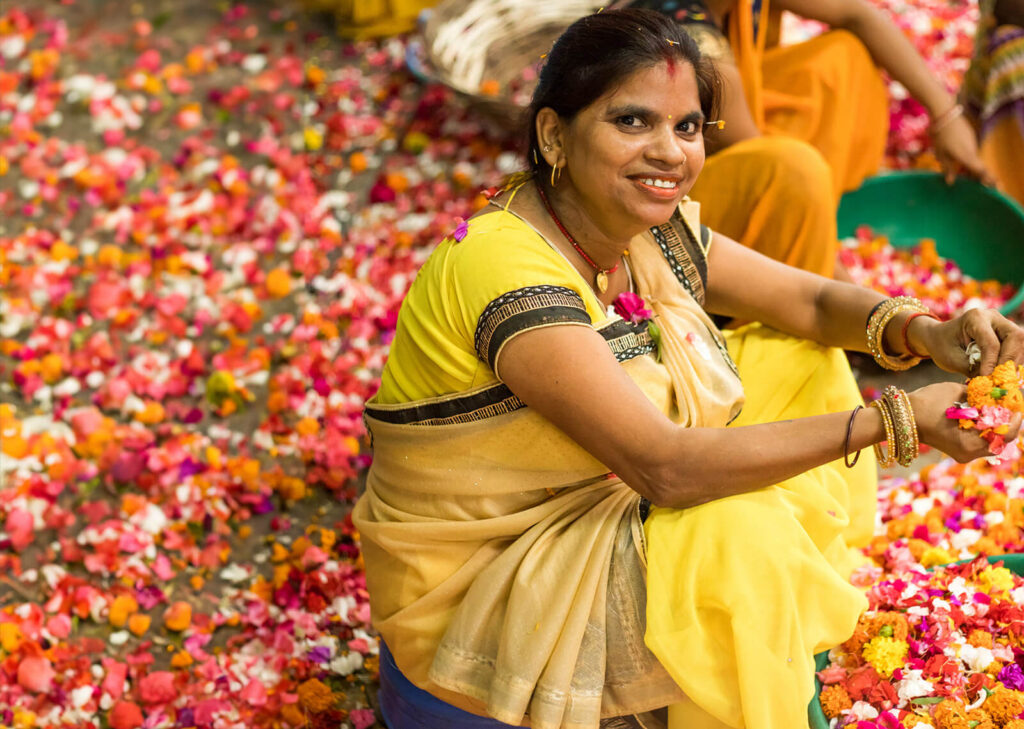 Smiling woman in a yellow sari sorting colorful flower petals.